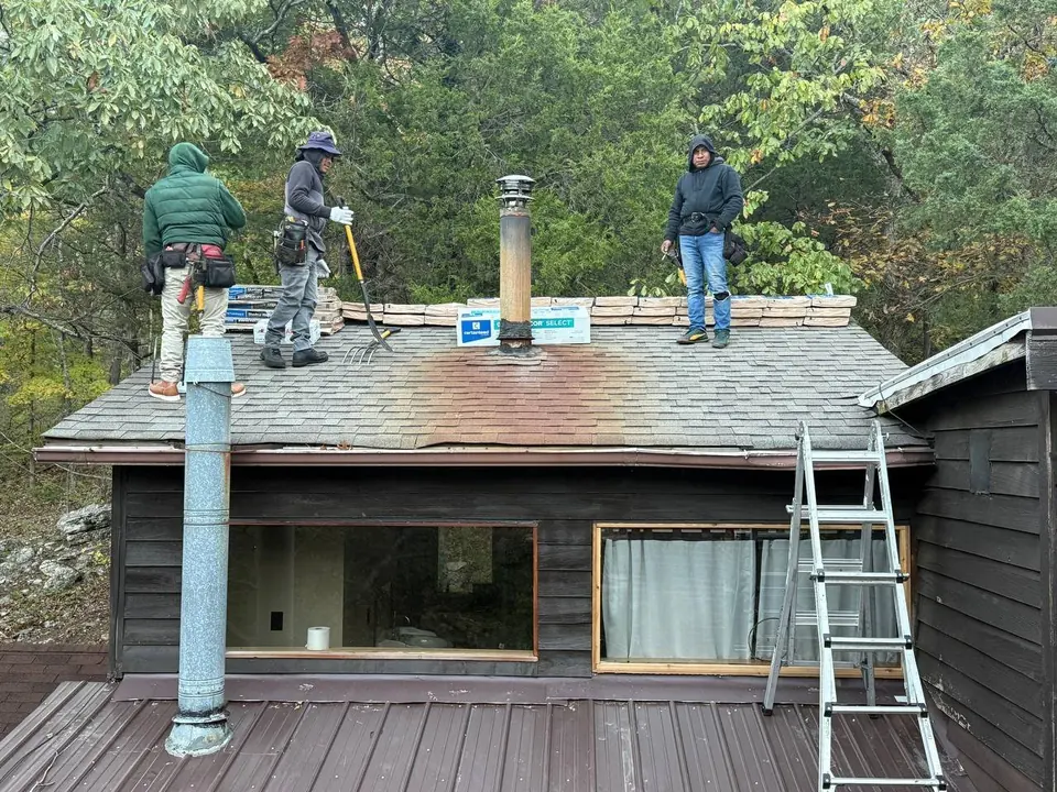 Roofing crew standing on an existing shingle roof beside staged materials